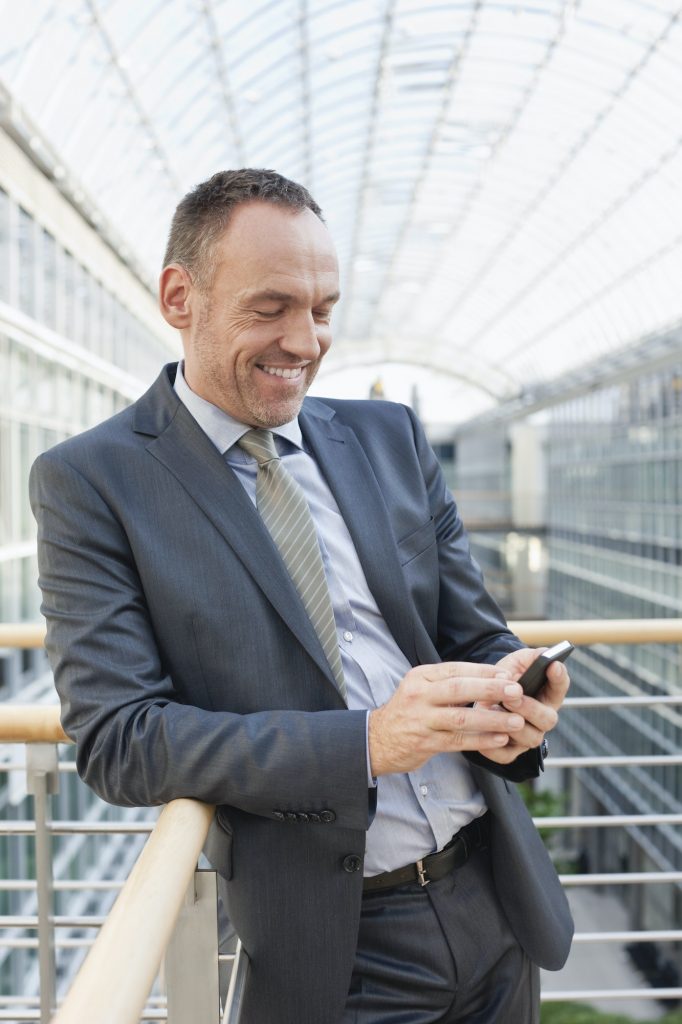 Germany, Leipzig, Businessman using cell phone, smiling